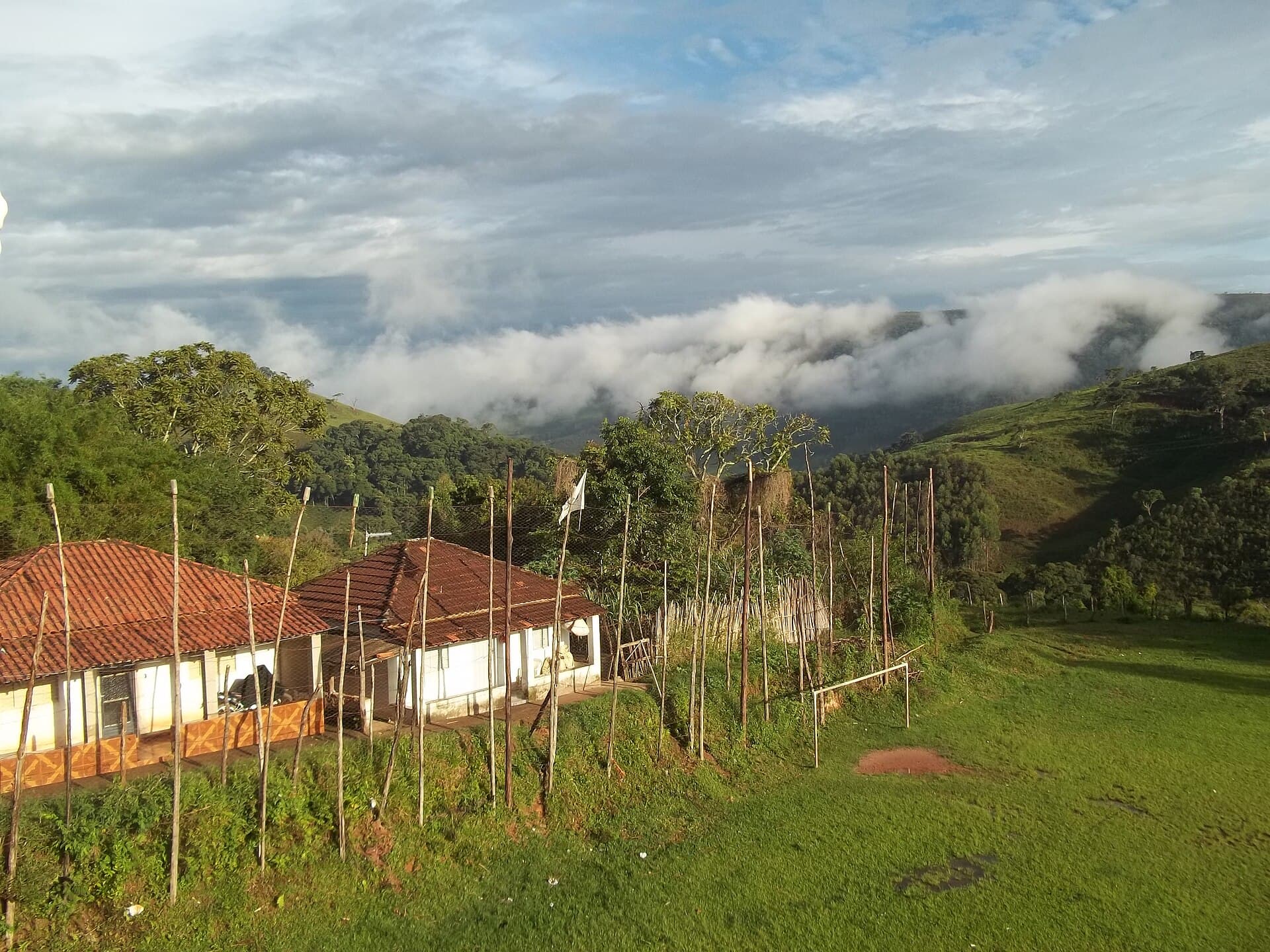 Casas rurais de telhado de barro entre morros com neblina, em Baependi, Minas Gerais