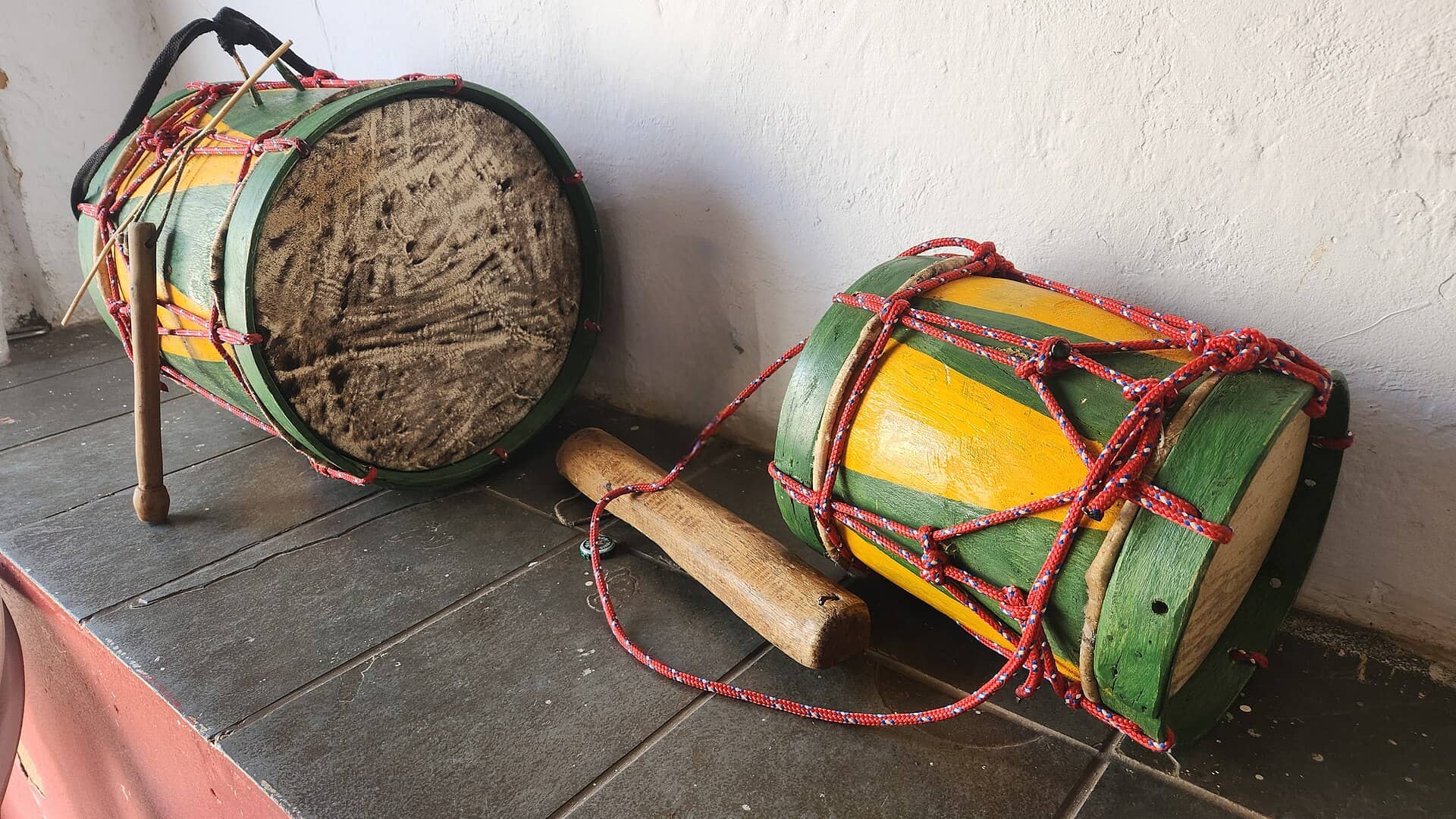 Dois tambores artesanais verdes e amarelos amarrados com corda vermelha, usados na Folia de Reis