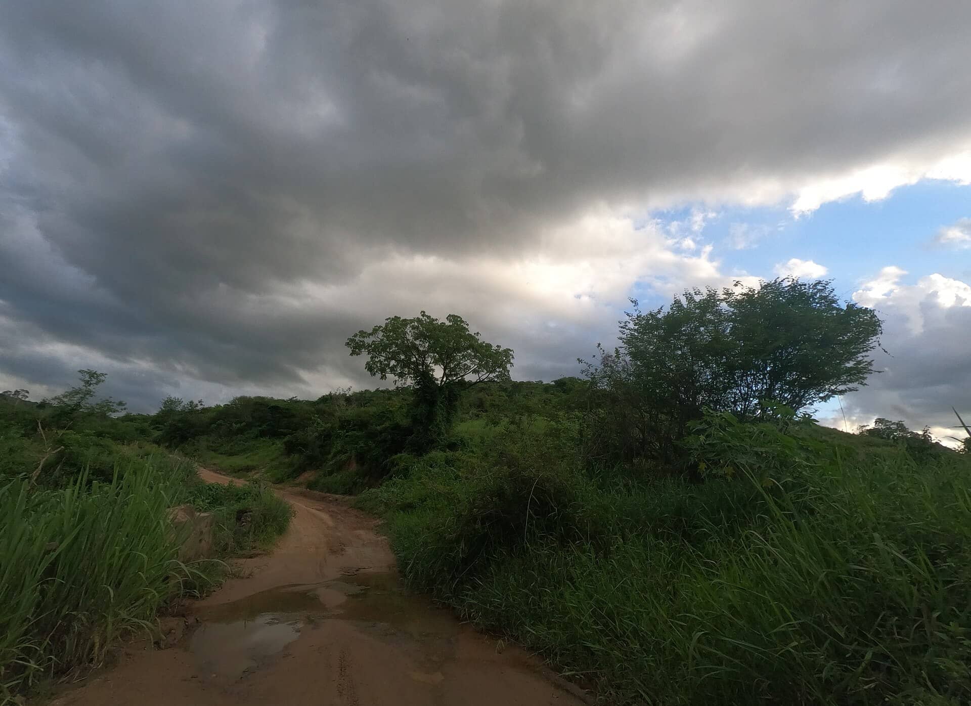 Estrada de terra com poça de lama sob céu carregado, em Rubim, Minas Gerais
