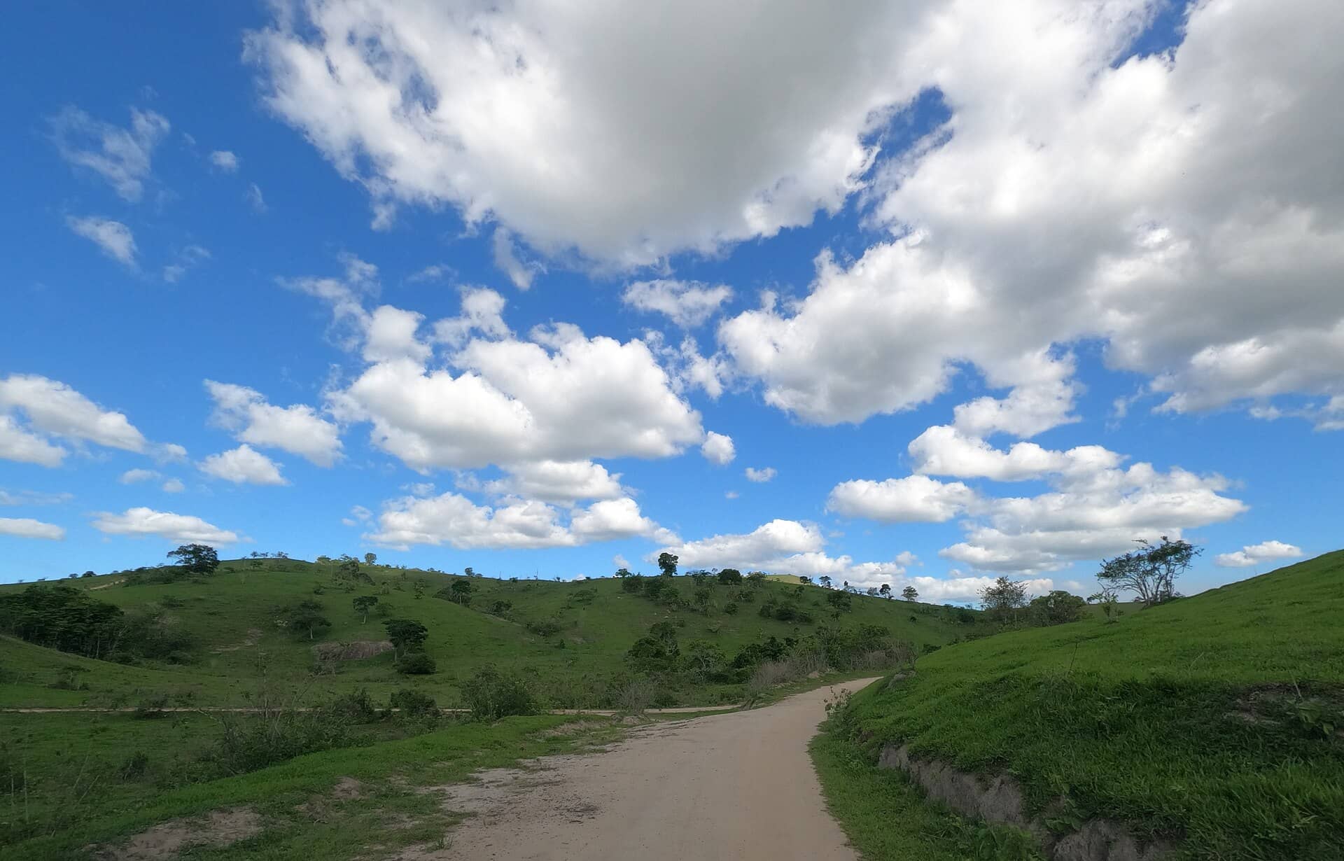 Estrada de terra entre morros verdes e céu com nuvens, em Palmópolis, Minas Gerais