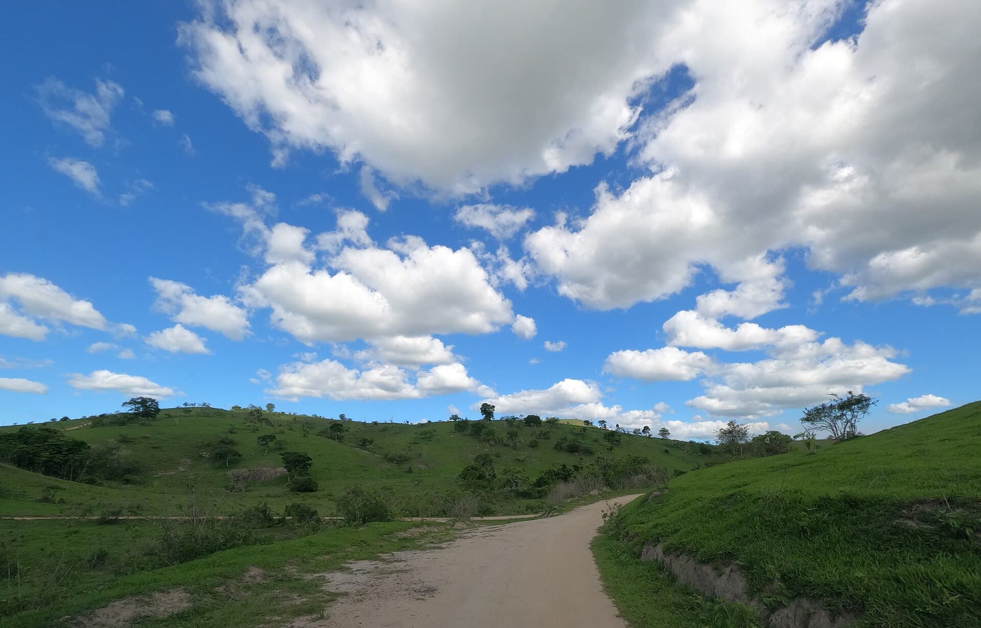 Estrada de terra entre morros verdes e céu com nuvens, em Palmópolis, Minas Gerais