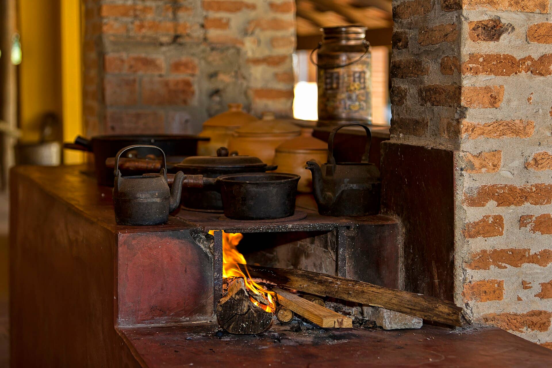 Fogão a lenha com panelas de ferro e chaleiras sobre a chapa, com fogo aceso, em cozinha de fazenda
