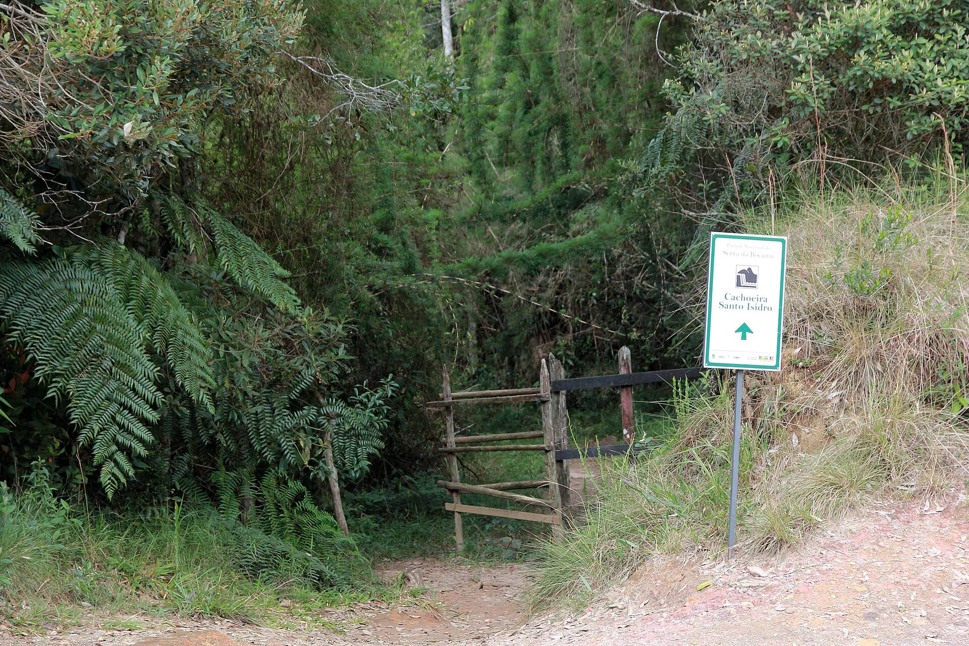 Início de trilha com porteira de madeira e placa indicando a Cachoeira Santo Isidro, no Parque Nacional da Serra da Bocaina