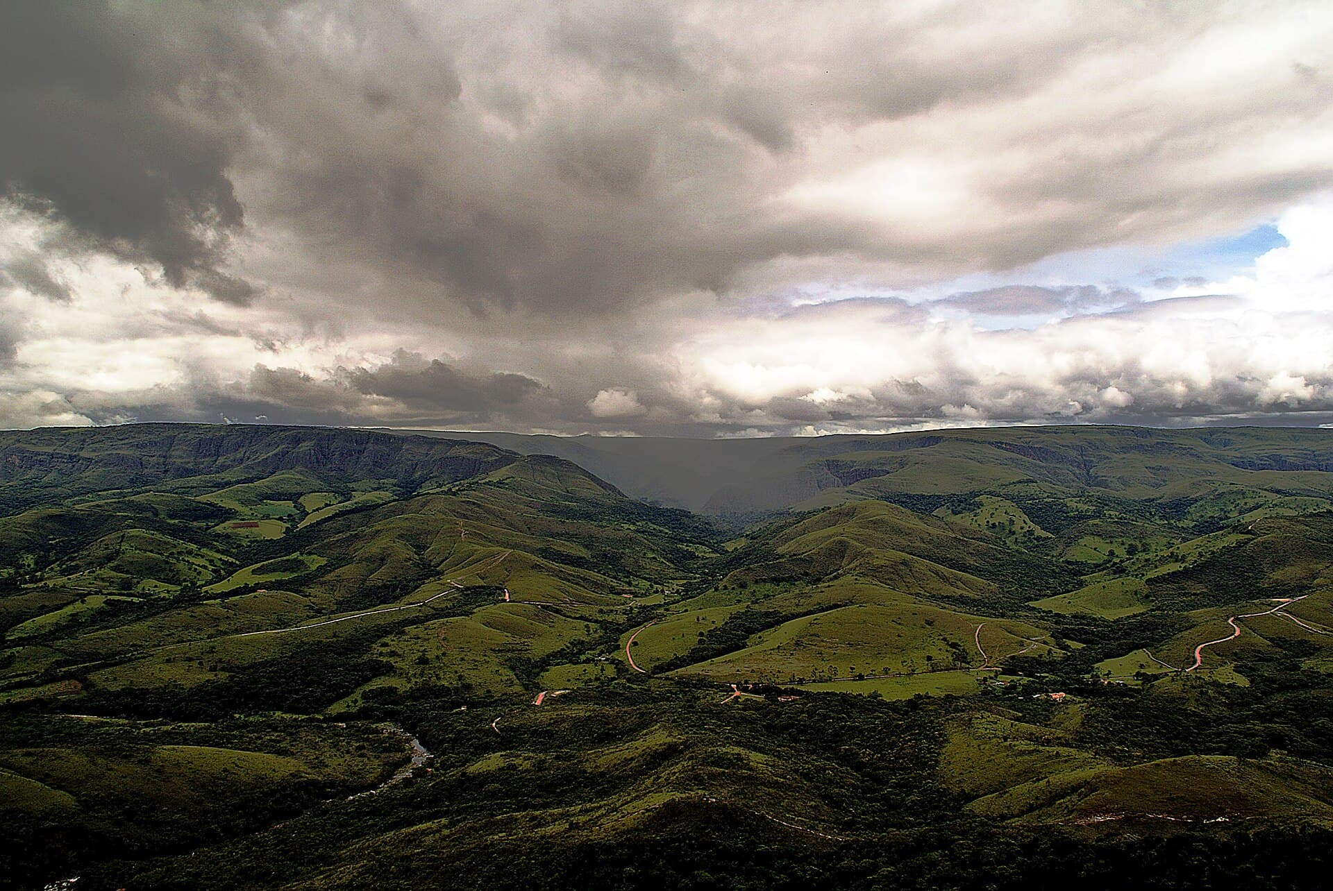 Morros verdes com estradas de terra sob nuvens carregadas, na Serra da Canastra